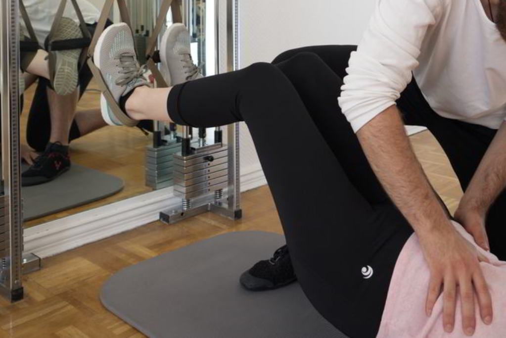 Eine Patientin liegt auf dem Rücken mit eingehängten Füßen in TRX-Schlaufen